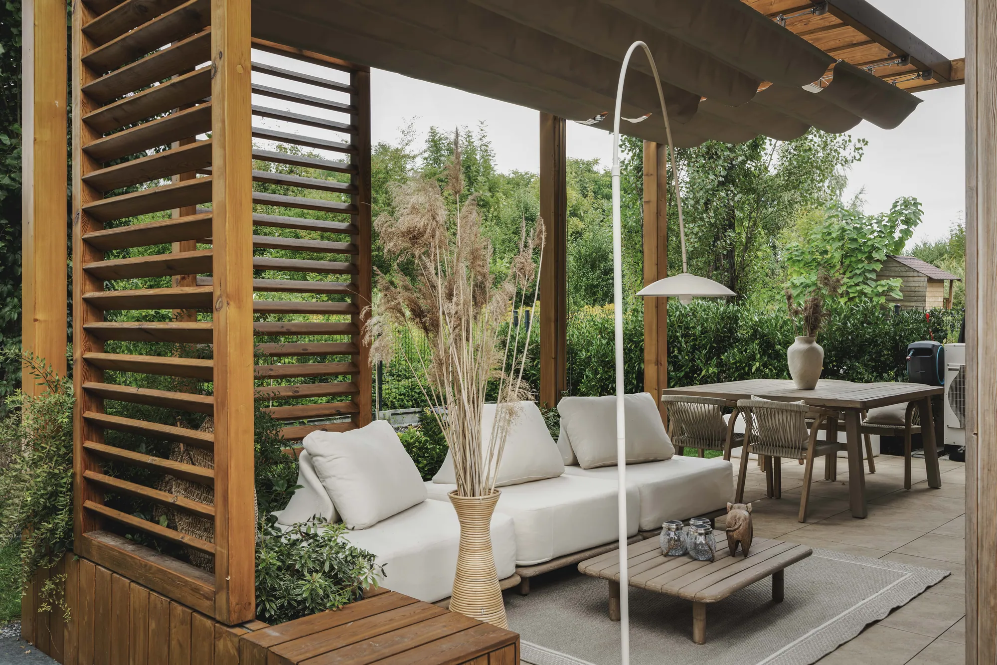 Drewniana pergola z lamelami i zadaszeniem z tkaniny nad tarasem z wypoczynkiem – w stylu śródziemnomorskim