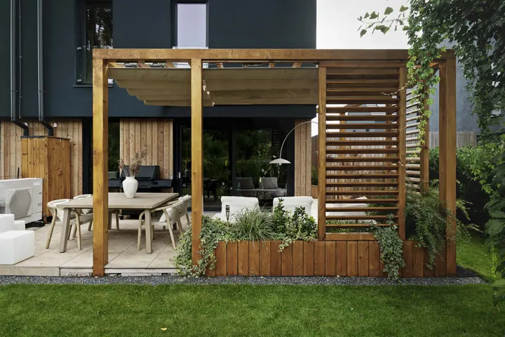 Drewniana pergola z lamelami, jadalnią i donicami z roślinami w ogrodzie